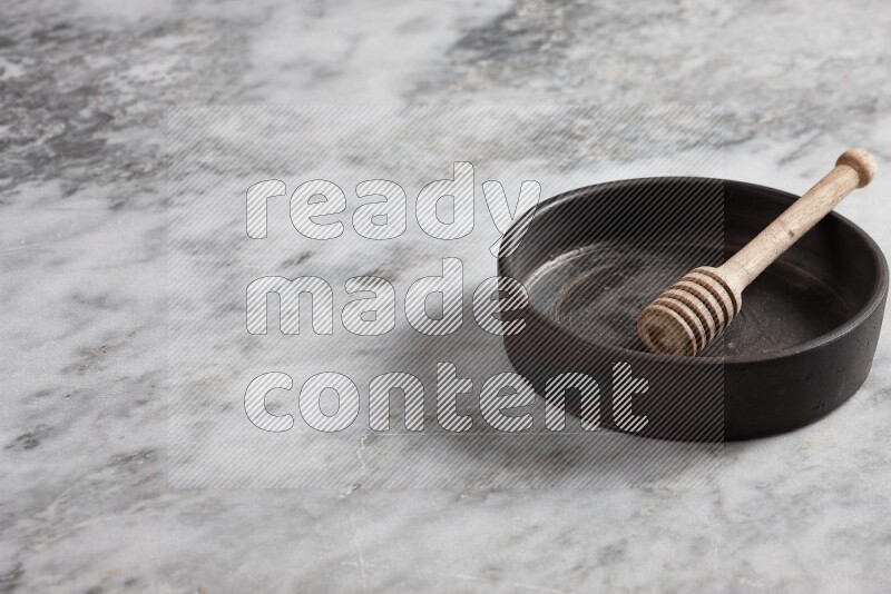 Black pottery oven plate with wooden honey dipper in it on grey marble background