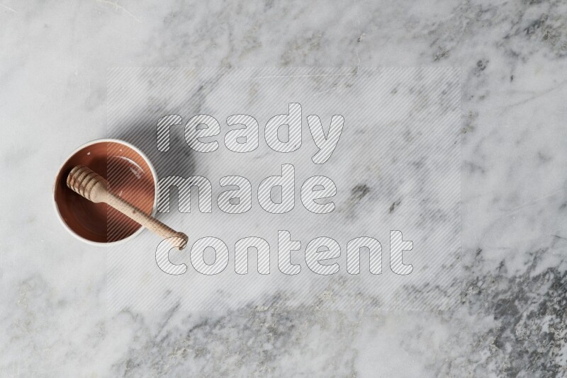 وعاء فخاري متعدد الألوان مع ملعقة عسل خشبية بداخله على خلفية من الرخام الرمادي