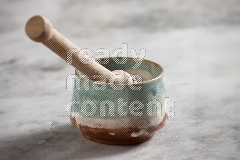 Multicolored pottery bowl with wooden honey dipper in it on grey marble background