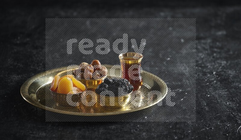 Dried fruits in metal bowls on a tray in a dark setup