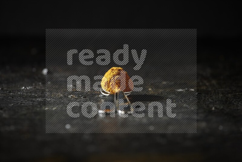 2 metal spoons full of turmeric powder on a textured black background