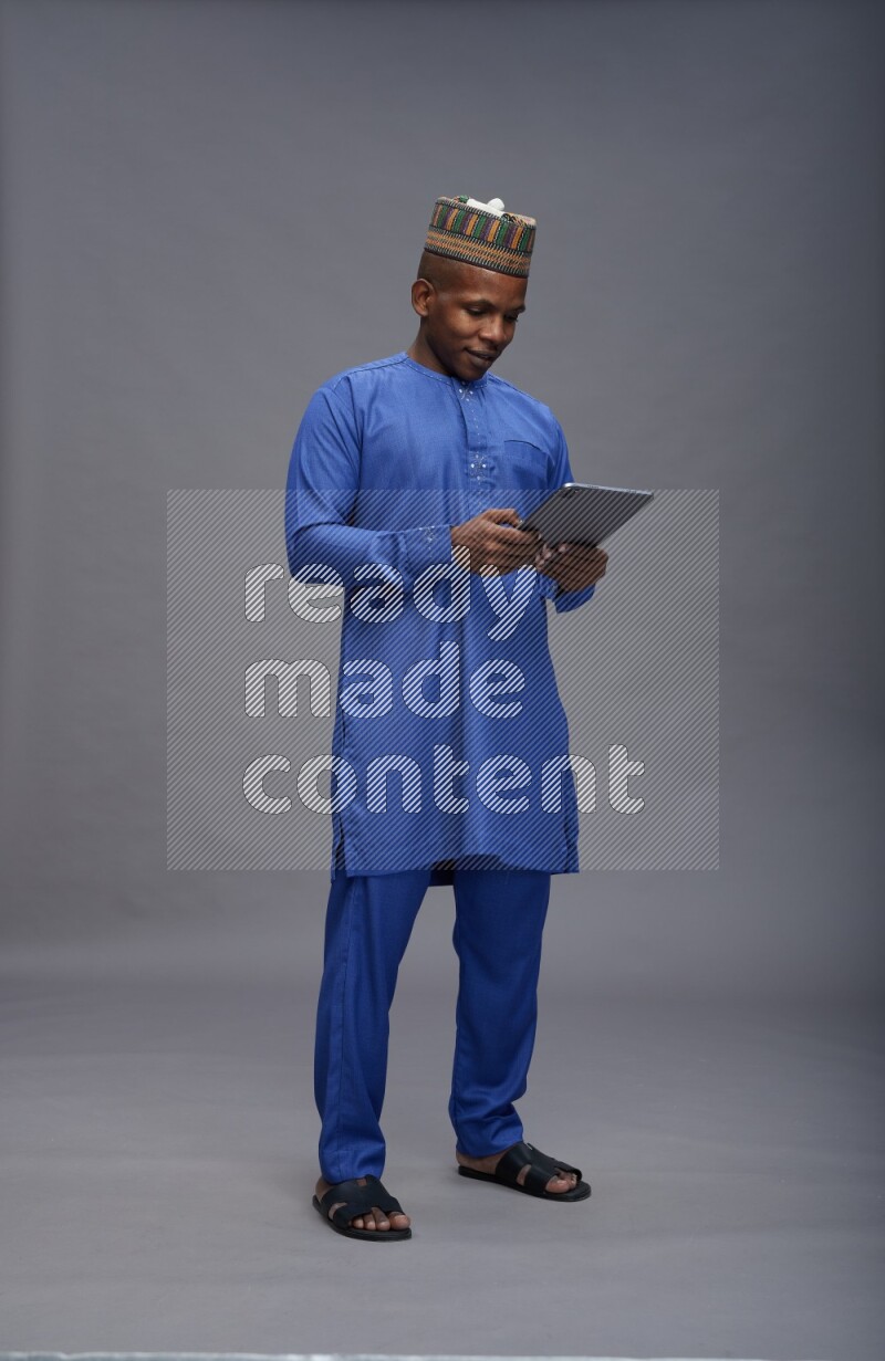Man wearing Nigerian outfit standing working on tablet on gray background