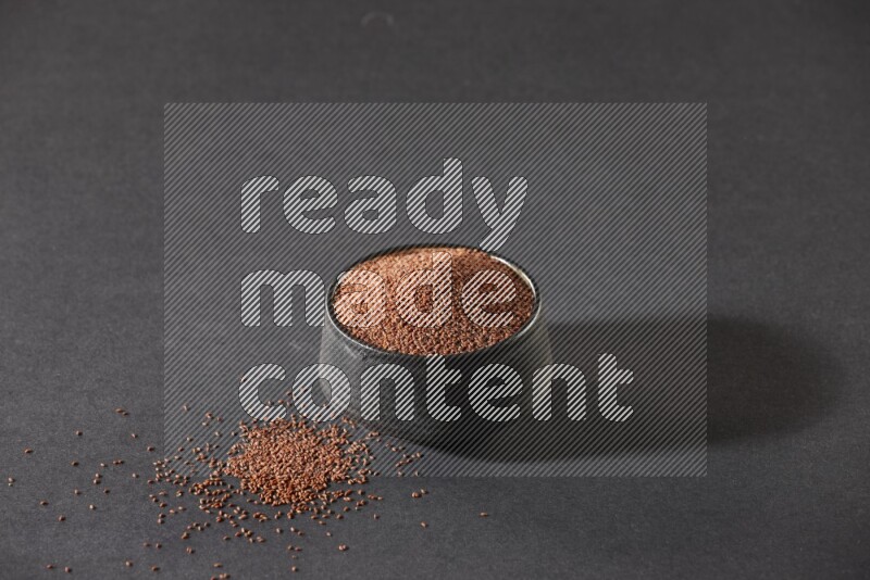 A black pottery bowl full of garden cress seeds on a black flooring