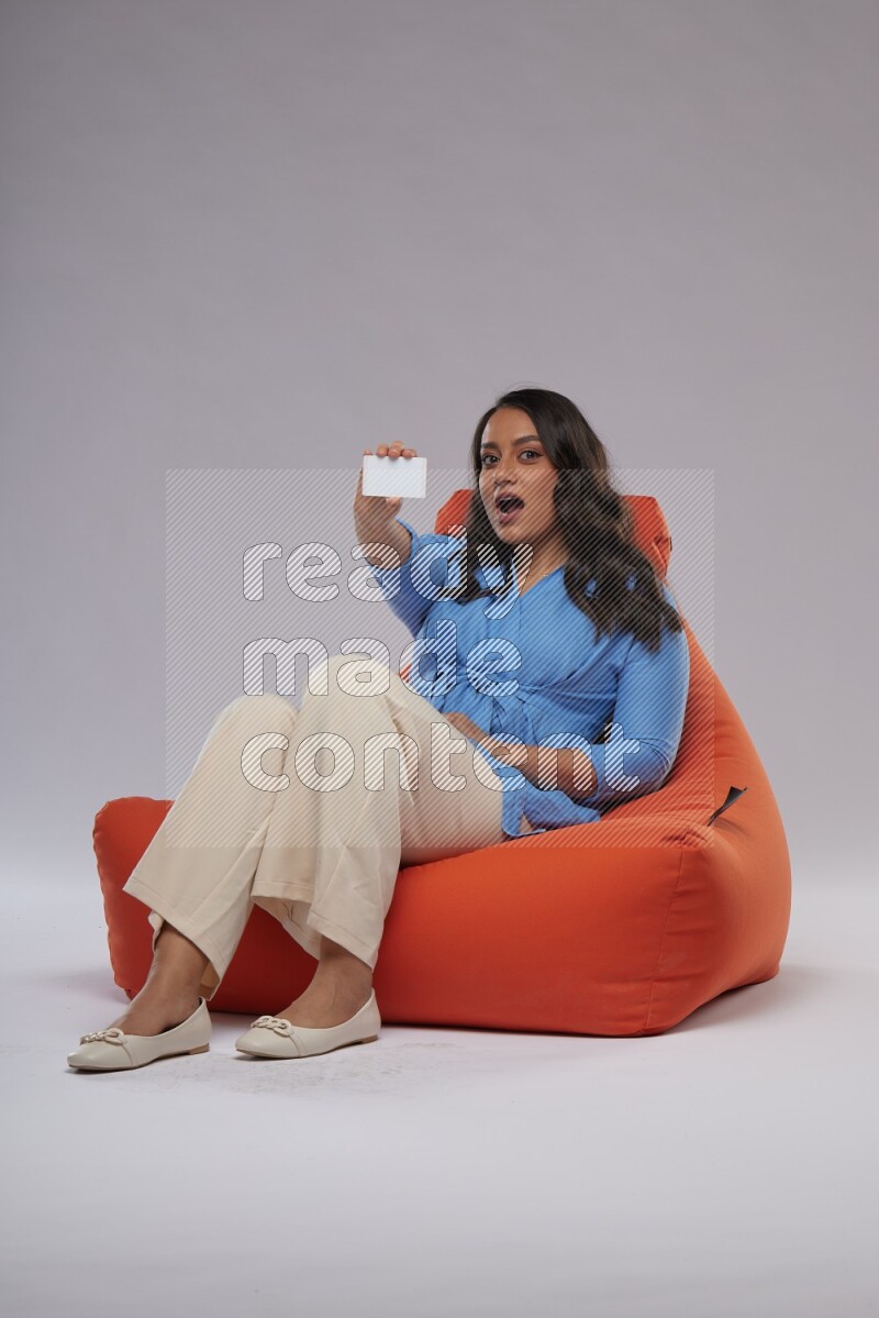 A woman sitting on an orange beanbag and holding ATM card