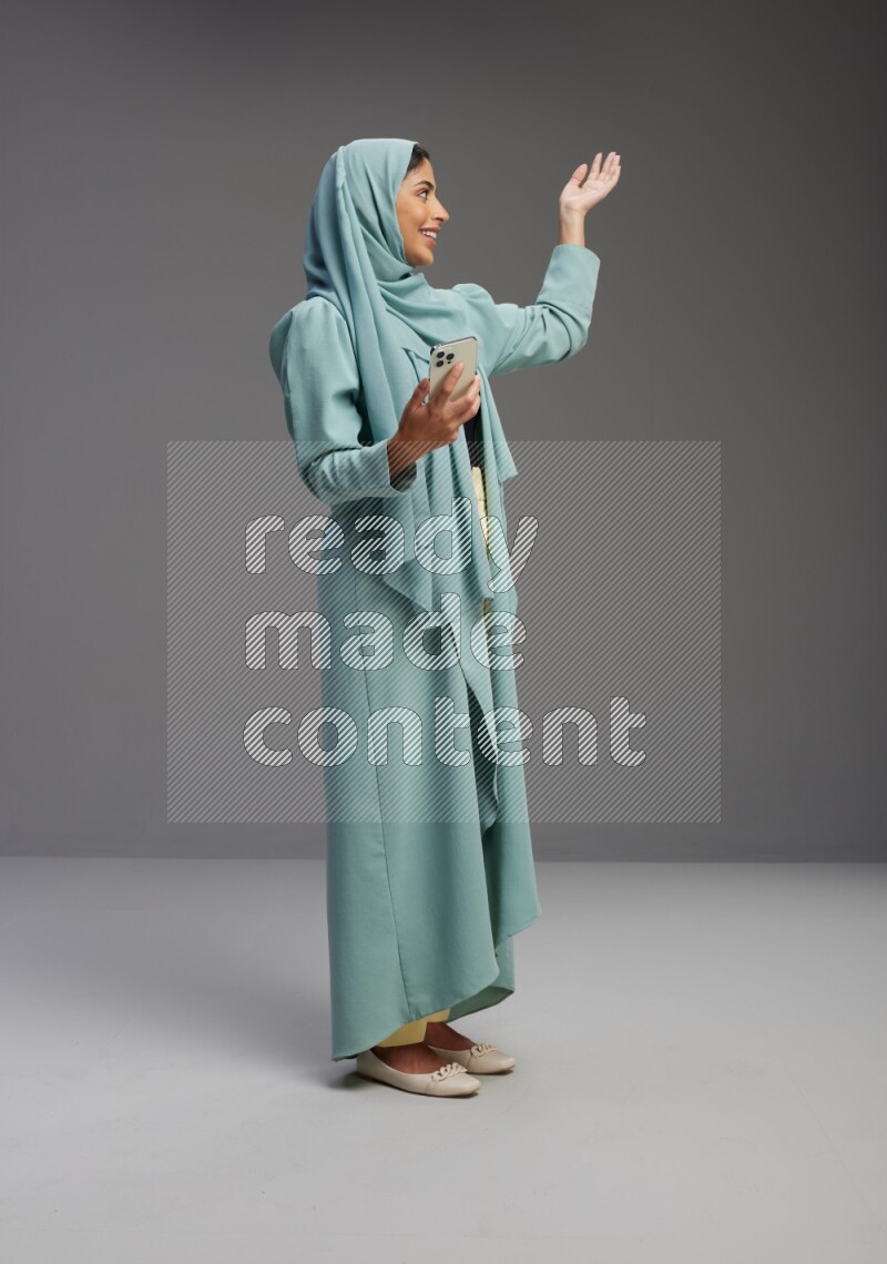Saudi Woman wearing Abaya standing texting on phone on Gray background