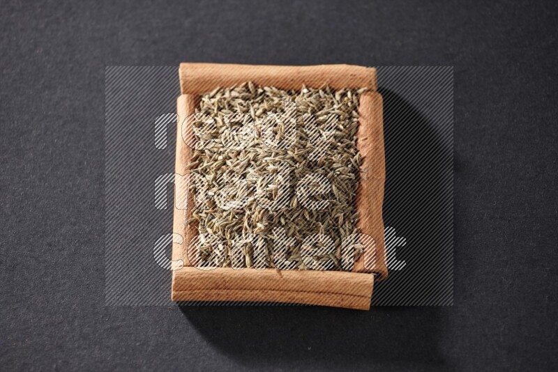A single square of cinnamon sticks full of cumin on black flooring
