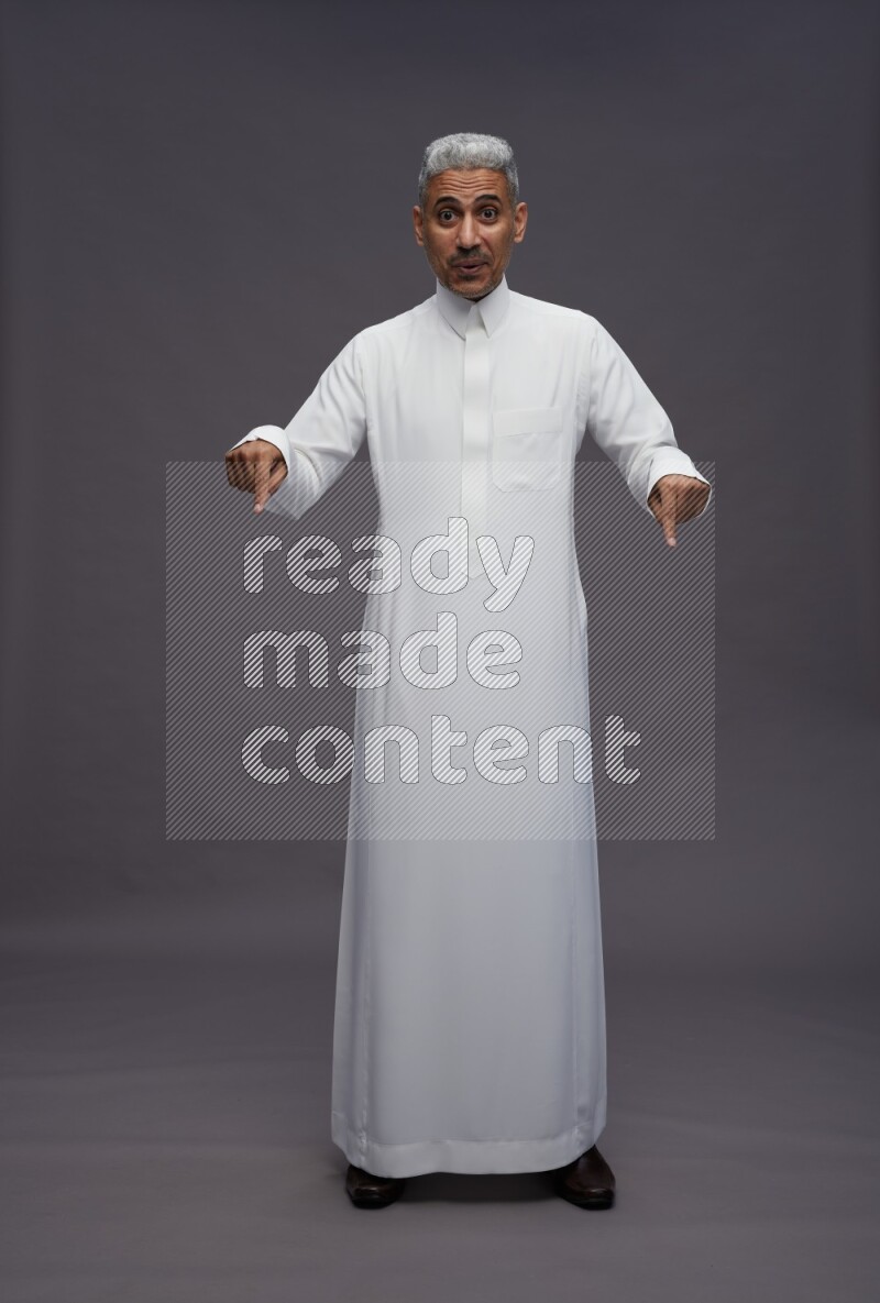 Saudi man wearing thob standing interacting with the camera on gray background