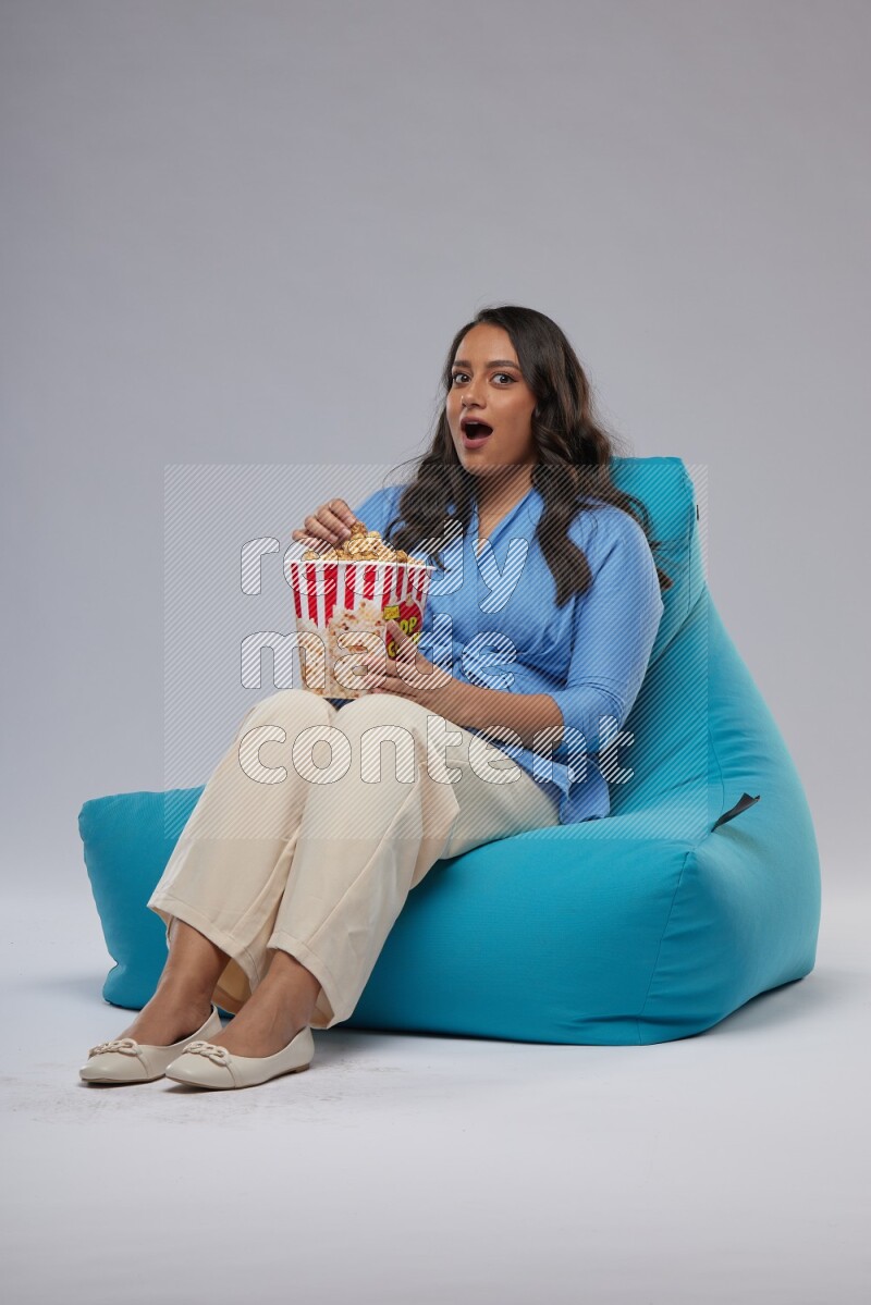 A woman sitting on a blue beanbag and eating popcorn