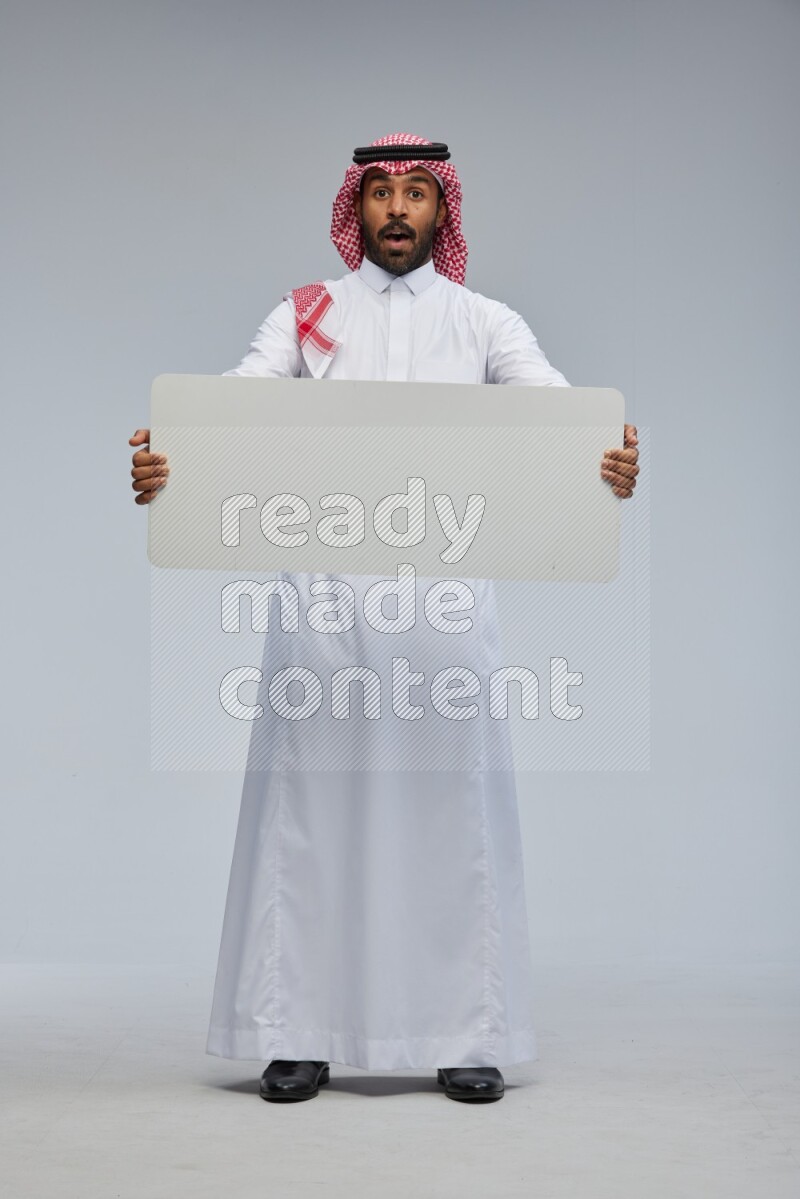 Saudi man Wearing Thob and shomag standing holding board on Gray background