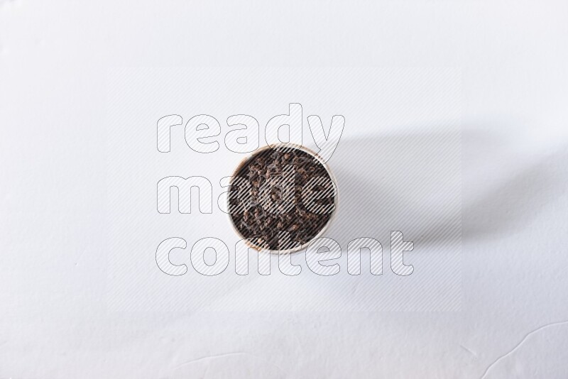 A beige ceramic bowl full of cloves on a white flooring