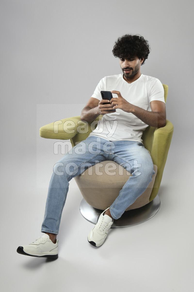 A man wearing casual sitting on a chair texting on the phone on white background