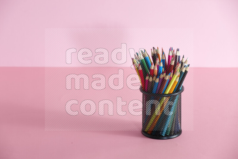Pens, pencils and other different school supplies in a metal pen holder on rose background