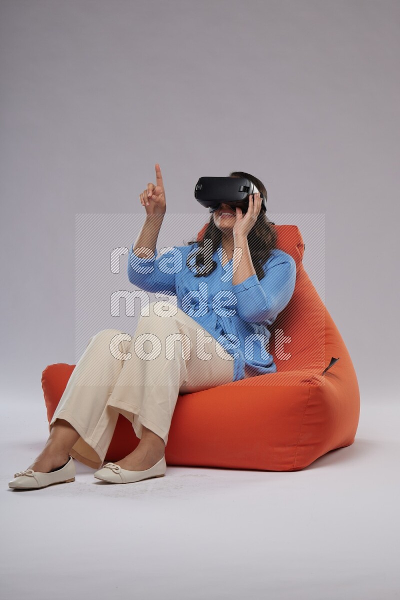 A woman sitting on an orange beanbag and gaming with VR