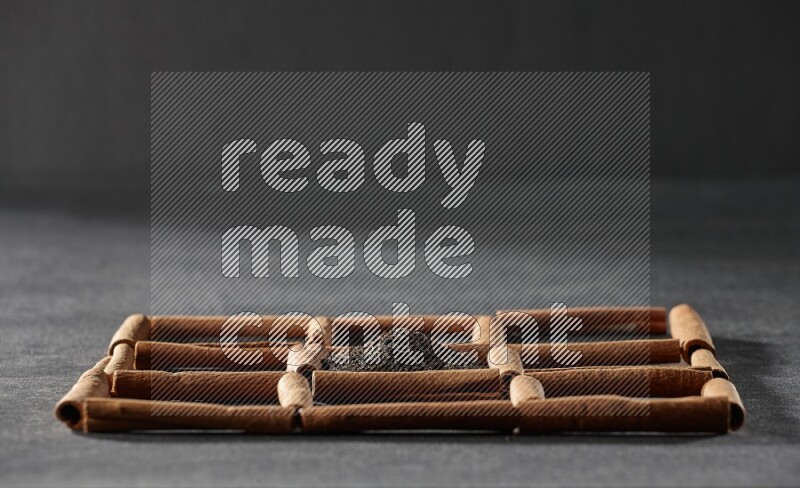 9 squares of cinnamon sticks full of tea in the middle surrounded by nutmeg, dried mint, cloves, dried basil, dried ginger, cinnamon, star anise and cardamom on black flooring