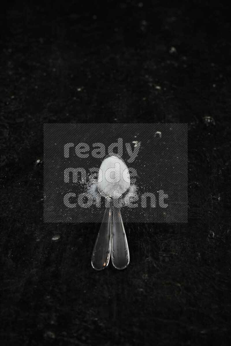 2 metal spoons filled with white salt on black background
