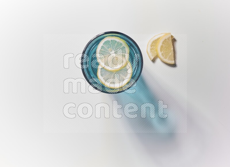 Blue transparent glass filled with blueberries decorated with lemon slices on a white background