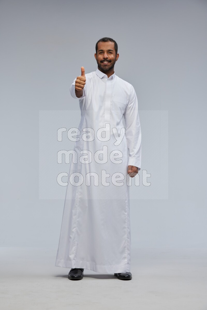 Saudi man Wearing Thob standing interacting with the camera on Gray background