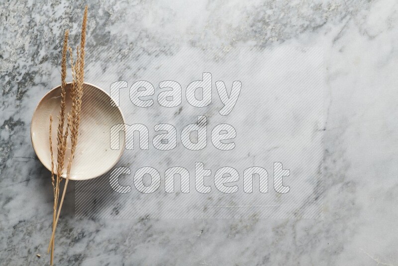 Wheat stalks on beige pottery plate on grey marble background