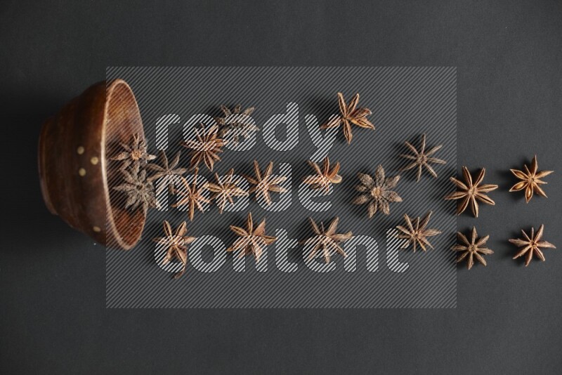Star anise lined out of wooden bowl across the frame on black background