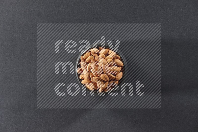 A black pottery bowl full of peeled almonds on a black background in different angles