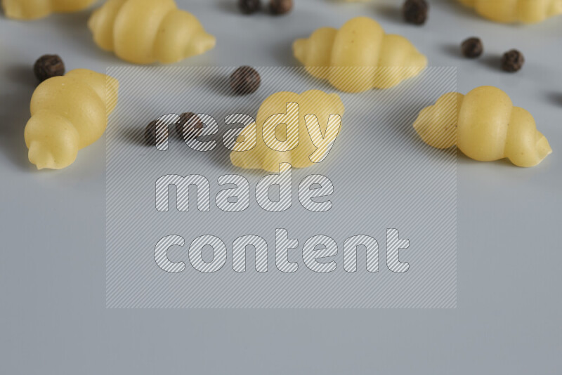 Raw pasta with different ingredients such as cherry tomatoes, garlic, onions, red chilis, black pepper, white pepper, bay laurel leaves, rosemary, cardamom and mushrooms on light blue background