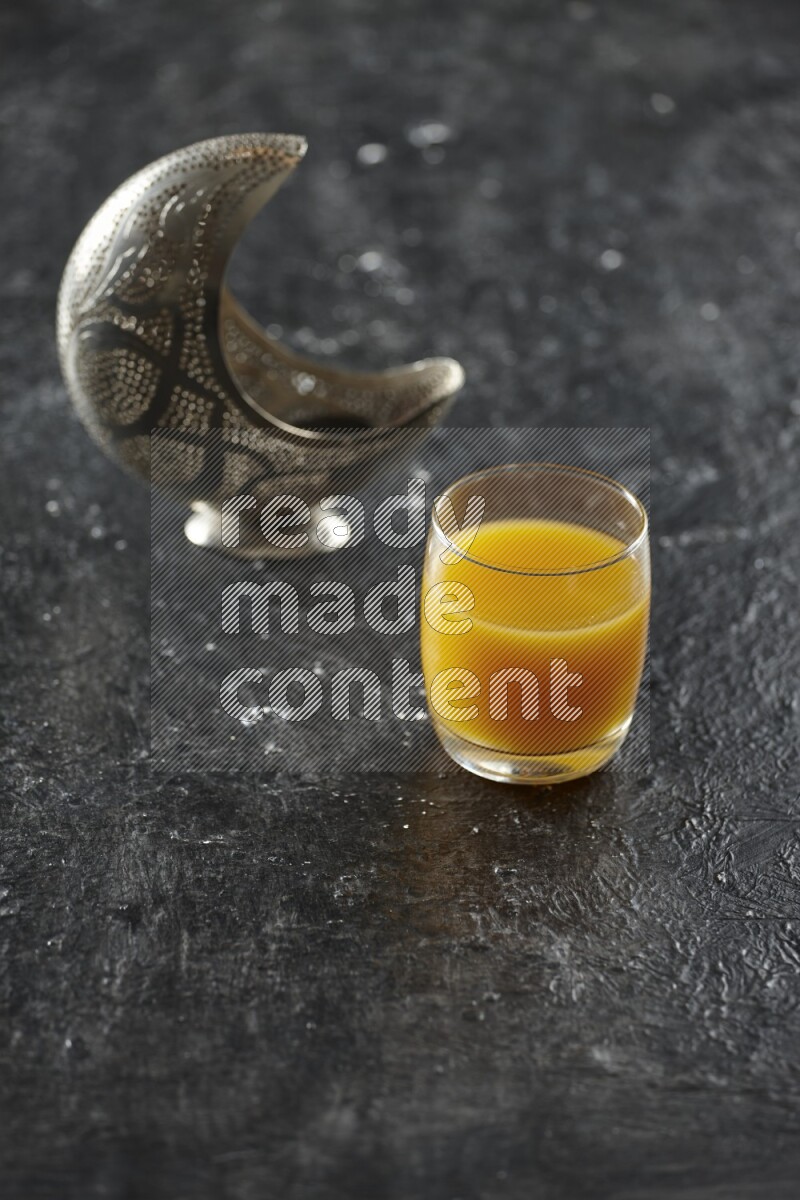 A silver lantern with different drinks, dates, nuts, prayer beads and quran on textured black background