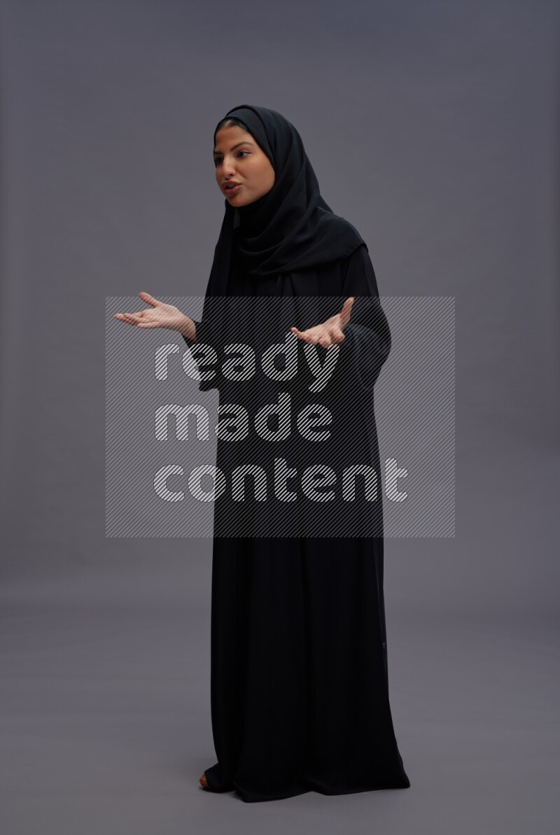 Saudi woman wearing Abaya standing interacting with the camera on gray background
