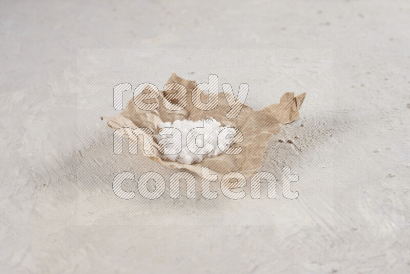 A crumpled piece of paper full of white salt on white background