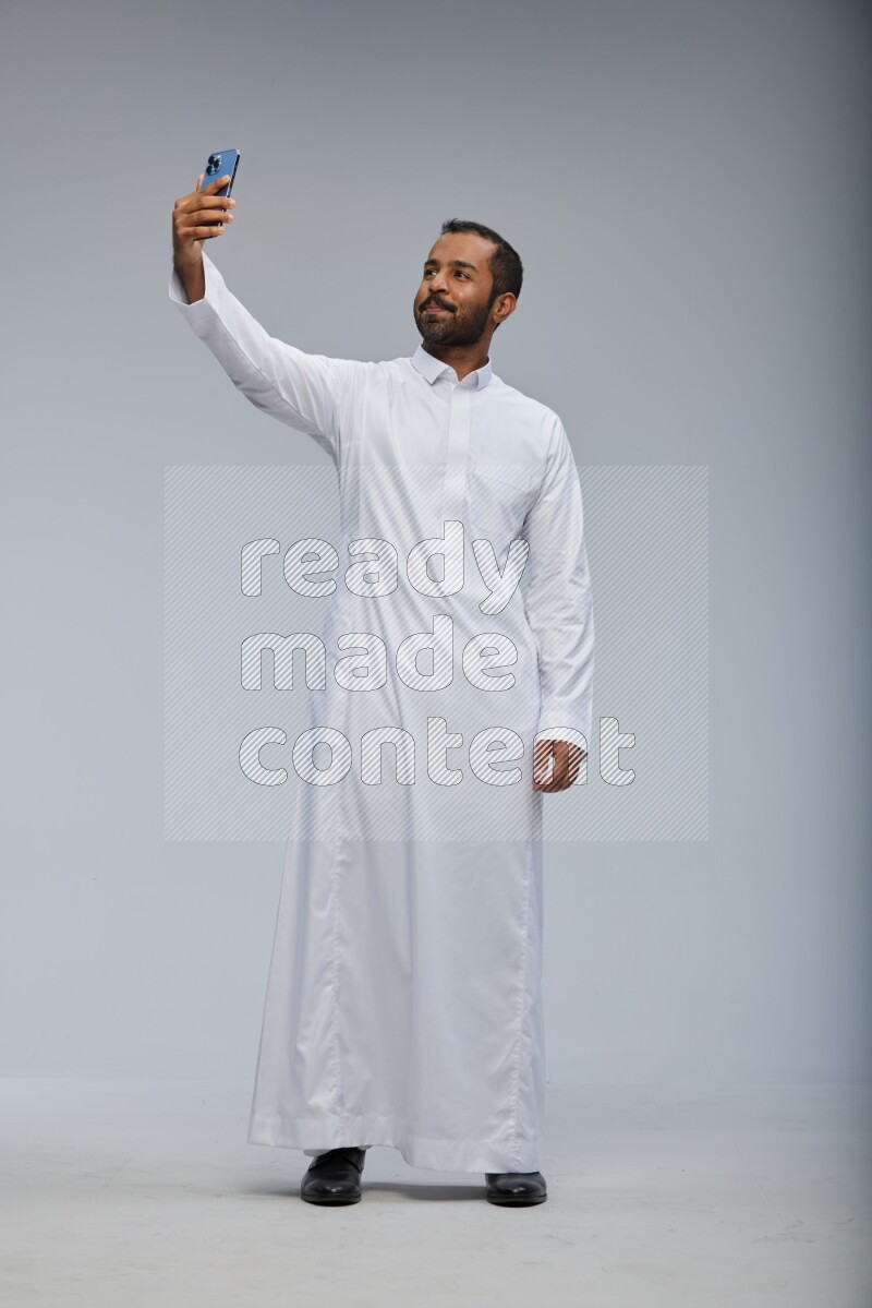 Saudi man wearing Thob standing taking selfie on Gray background