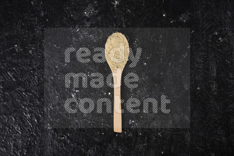 A wooden spoon full of ground ginger powder on black background