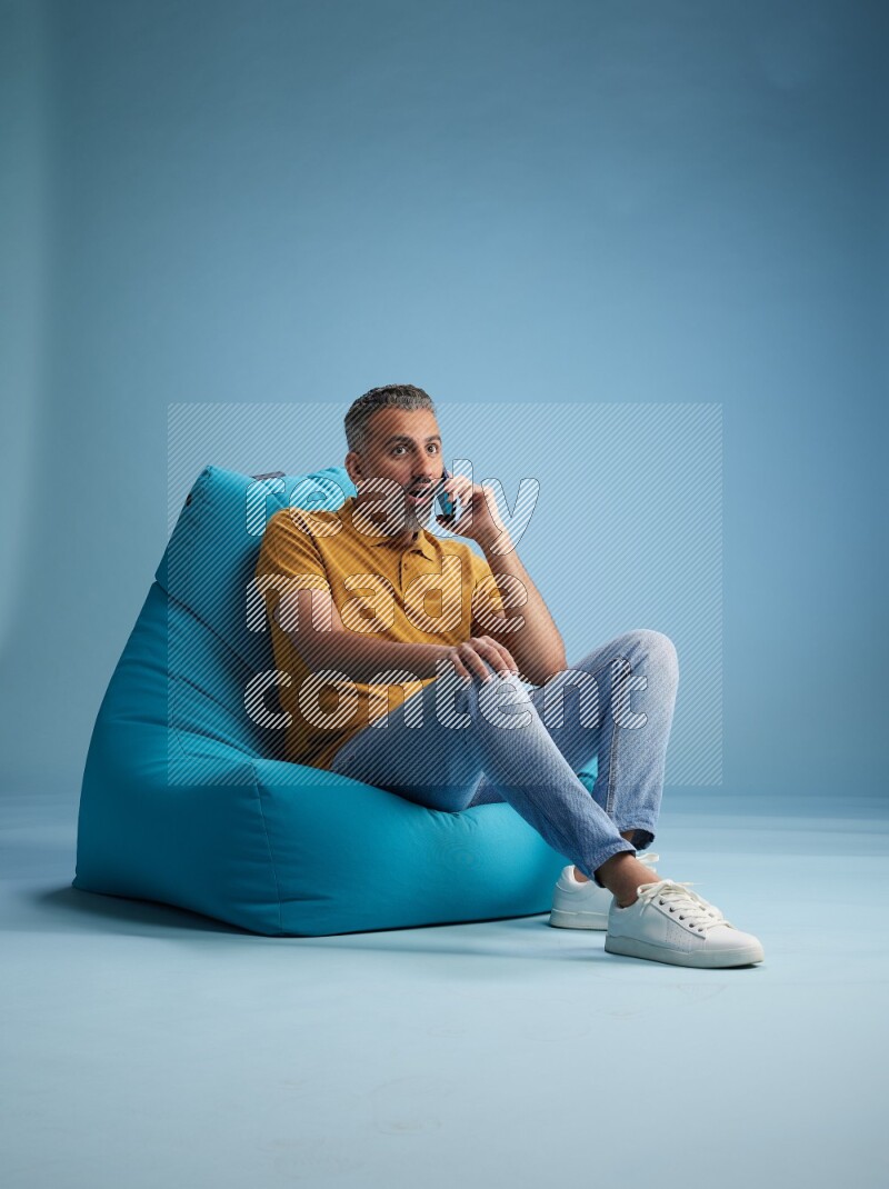 A man sitting on a blue beanbag and talking on the phone