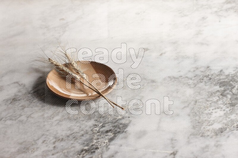 Wheat stalks on multicolored pottery plate on grey marble background