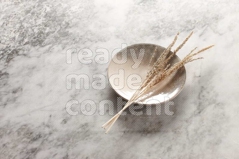 Wheat stalks on multicolored pottery plate on grey marble background