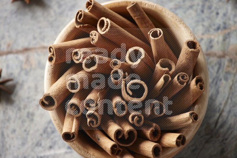 wooden bowl full of cinnamon sticks surrounded by star anis on marble background in different angles