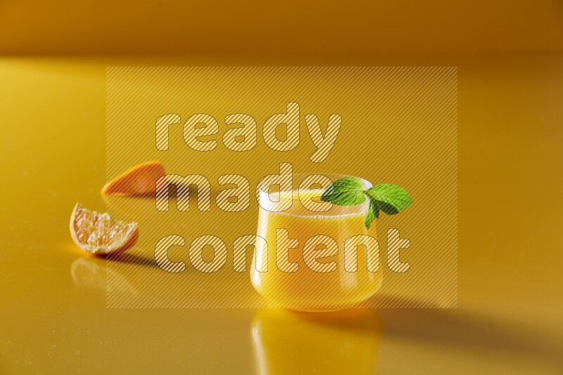 glass of orange juice with  mint on yellow background