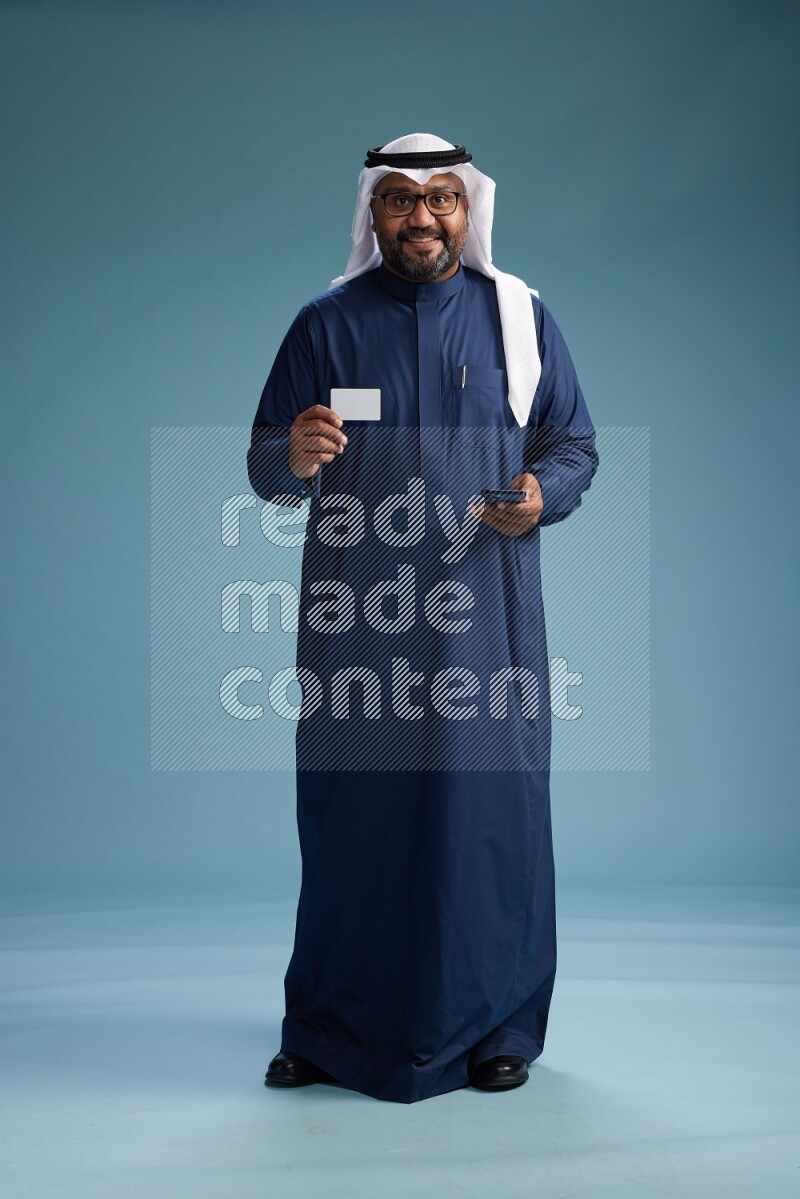 Saudi Man with shimag Standing holding ATM card while talking on phone on blue background