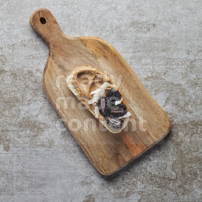 open faced peanut butter sandwich with blackberries  and coconut flakes on a  grey textured background