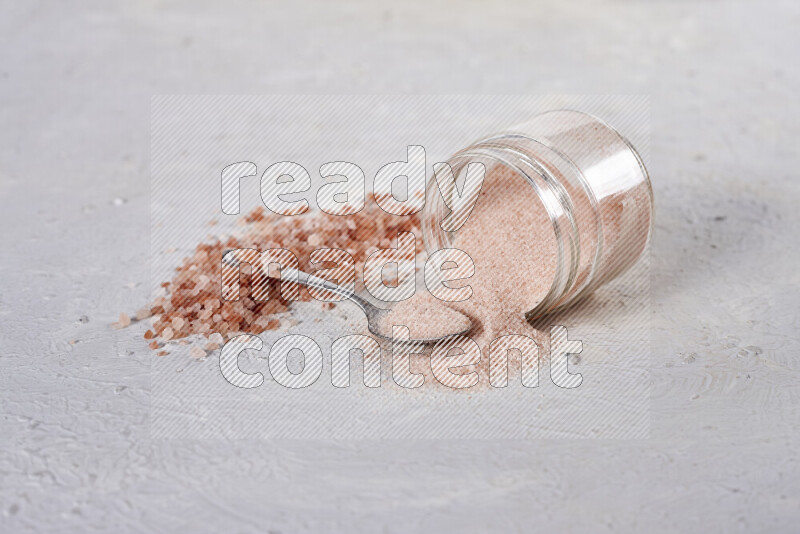 A glass jar full of fine himalayan salt with some himalayan crystals beside it on a white background