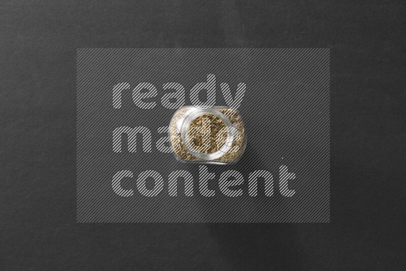 A glass spice jar full of cumin on black flooring