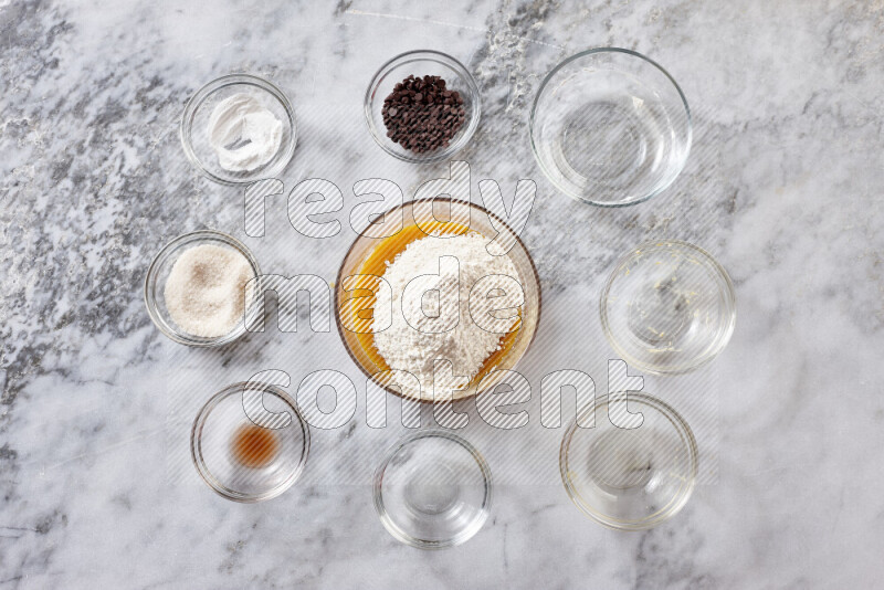 كوكيز خطوة بخطوة بمكوناتها، الدقيق، الزبدة، السكر البني، البيض، الفانيليا، السكر الأبيض، رقائق الشوكولاتة وصودا الخبز على خلفية رخام رمادي