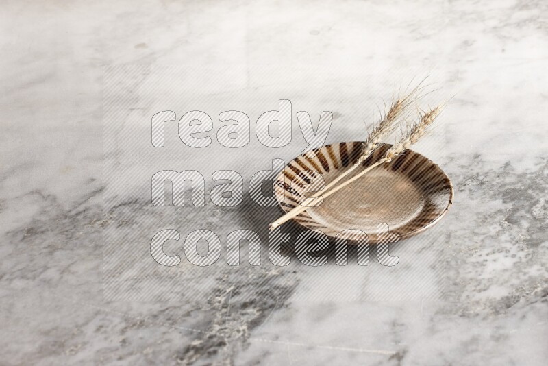 Wheat stalks on multicolored pottery plate on grey marble background