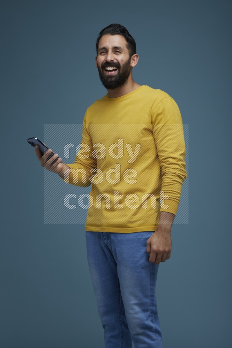 Man posing with a phone in a blue background wearing a yellow shirt