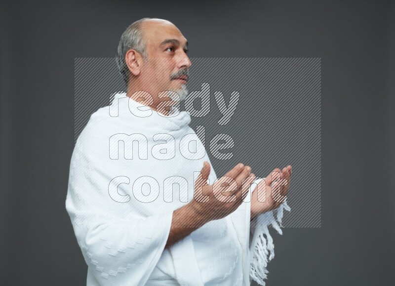 A man wearing Ehram Standing dua'a on gray background