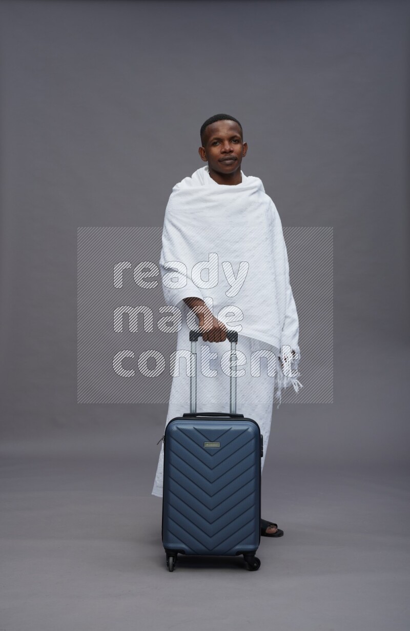 A man wearing Ehram Standing holding traveling bag on gray background