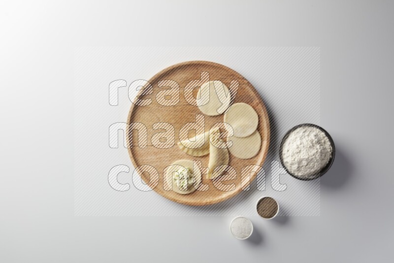 two closed sambosas and one open sambosa filled with cheese while flour, salt, and black pepper aside in a wooden dish on a white background