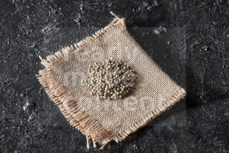 White pepper beads on a burlap piece of fabric on textured black flooring
