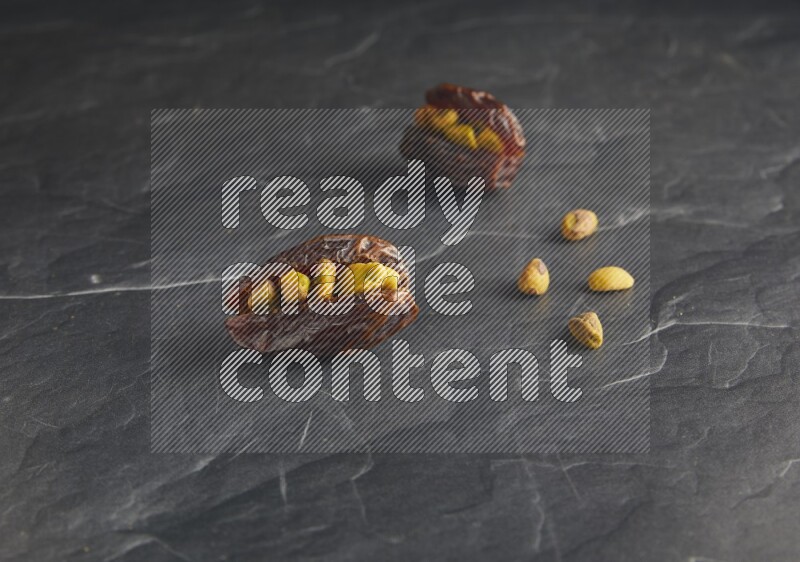 two pistachios stuffed madjoul dates on a black textured background