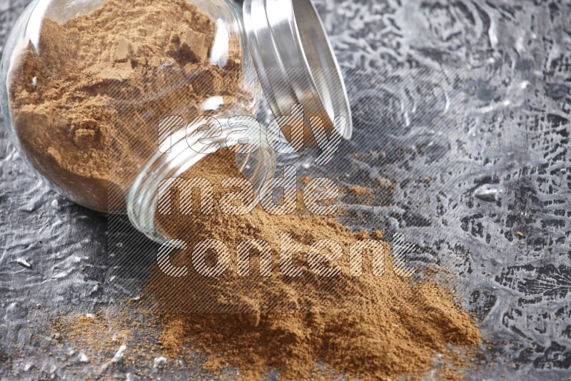 Flipped herbal glass jar full of cinnamon powder on textured black background