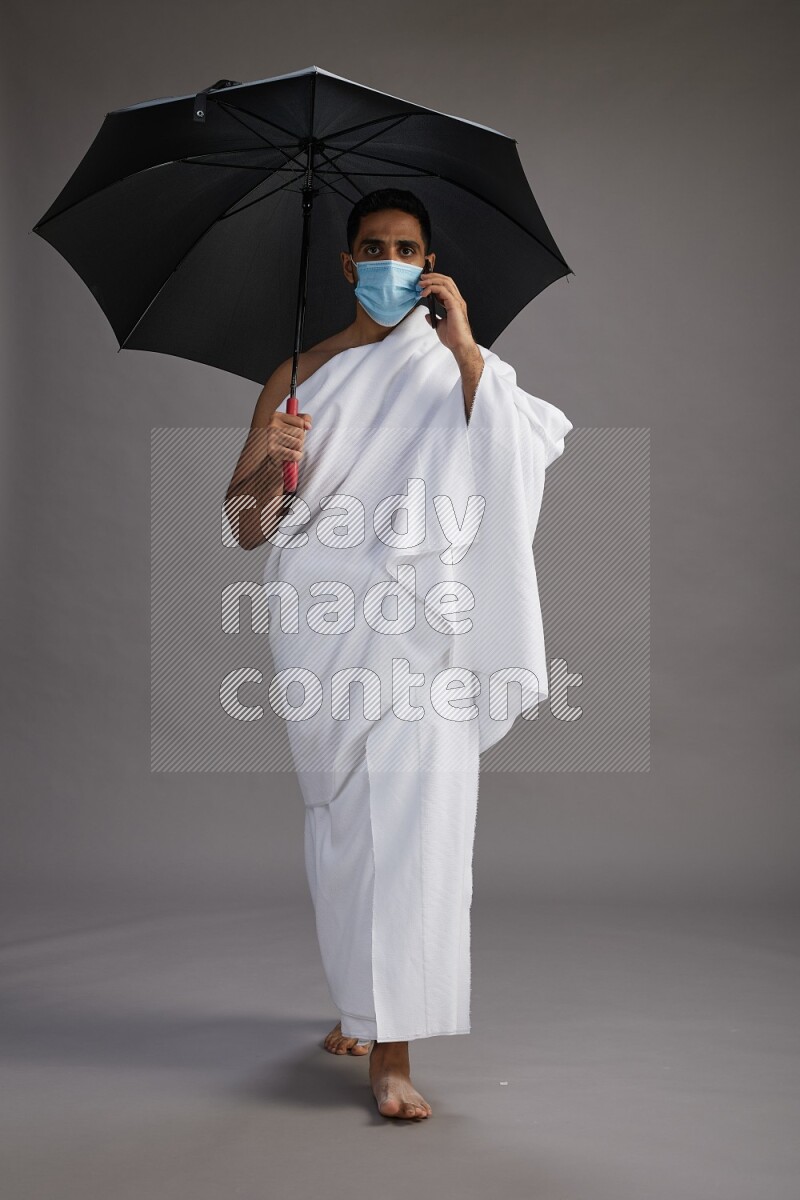 A man wearing Ehram and mask Standing holding umbrella on gray background on gray background