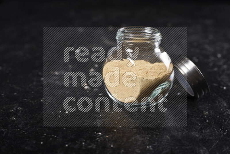 A glass jar full of ground ginger powder on black background